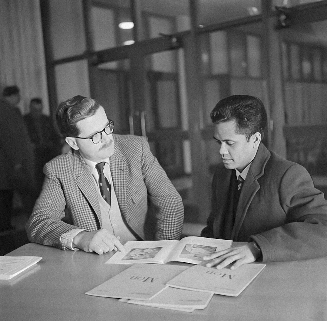 Two Portuguese colleagues reviewing a script together in a podcast studio